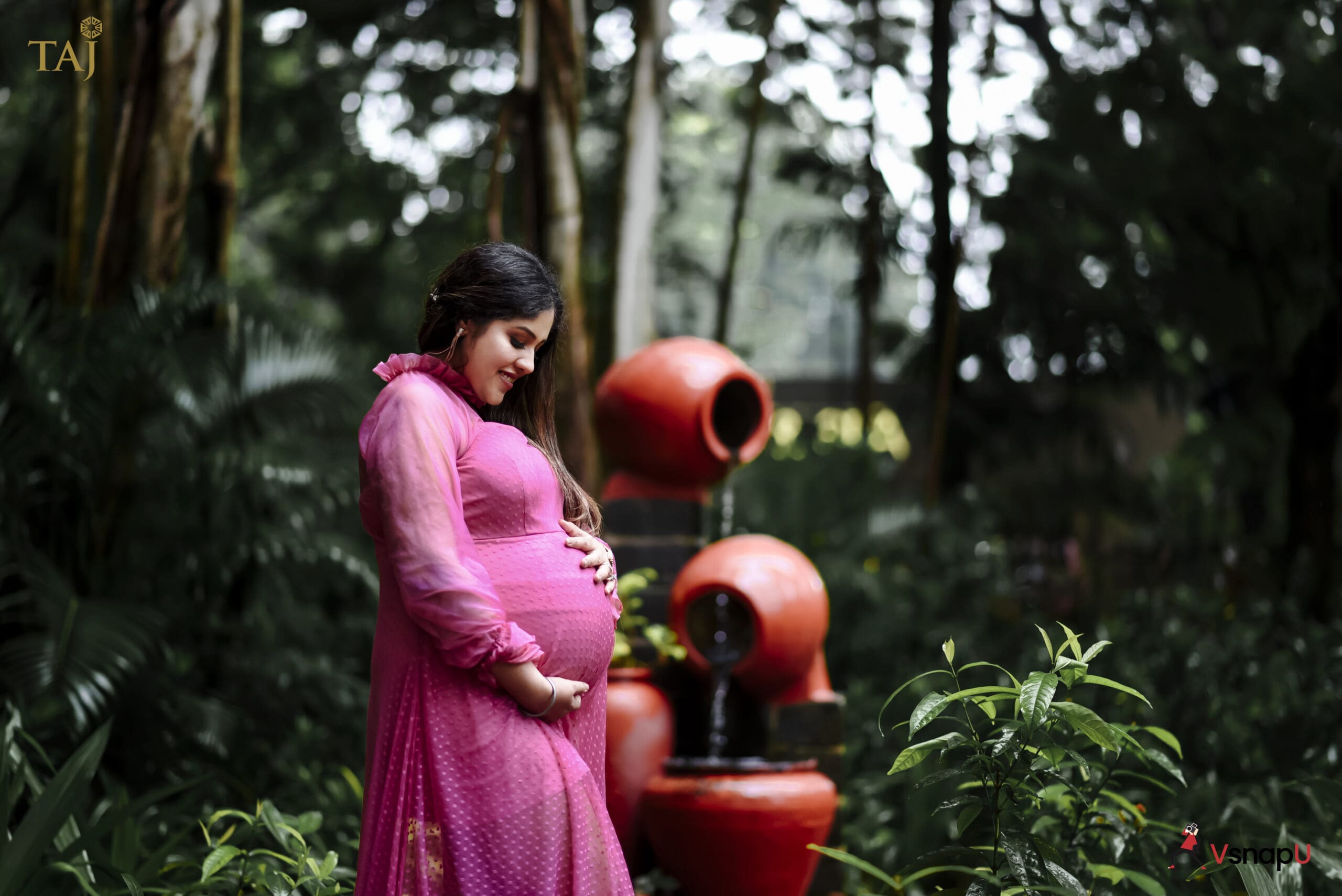 Maternity elegance captured with a woman in pink embracing her baby bump near a fountain.